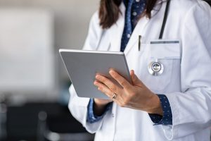 Close up of woman doctor hands using digital tablet at clinic. Closeup of female doctor in labcoat and stethoscope holding digital tablet, reading patient report. Hands holding medical report, copy space.