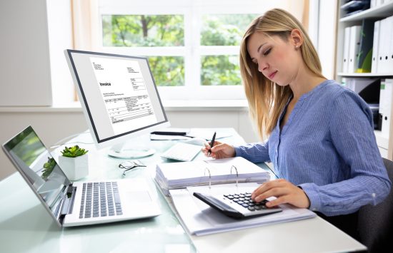 Young Businesswoman Calculating Bill With Computer And Laptop On Desk